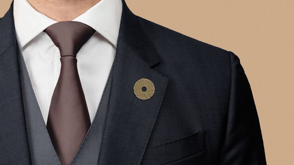 Close-up of a tailored suit and tie featuring a gold circular lapel pin with intricate design.