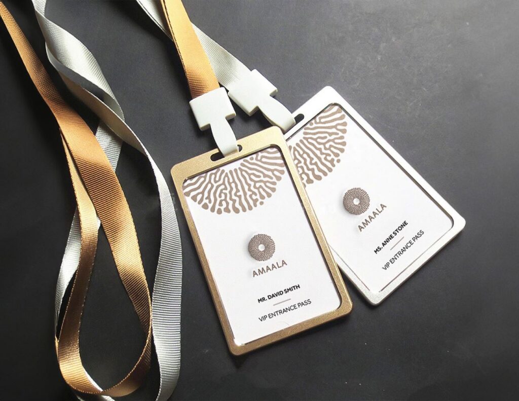 Two luxury AMAALA branded access badges with gold and white detailing, attached to satin ribbons.