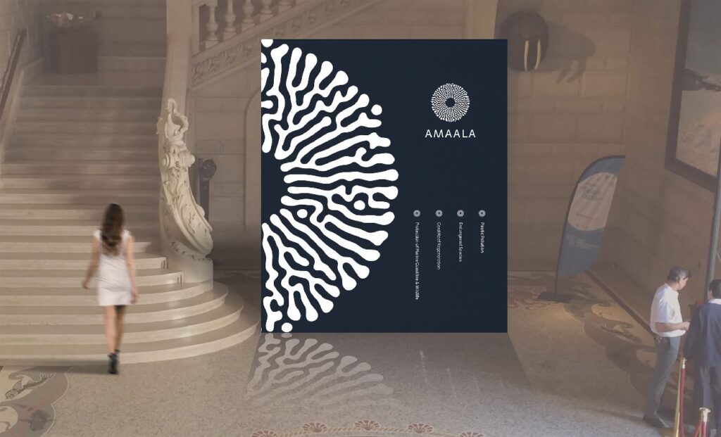 Large AMAALA branded display panel inside an elegant interior with a staircase and a person walking in the background.