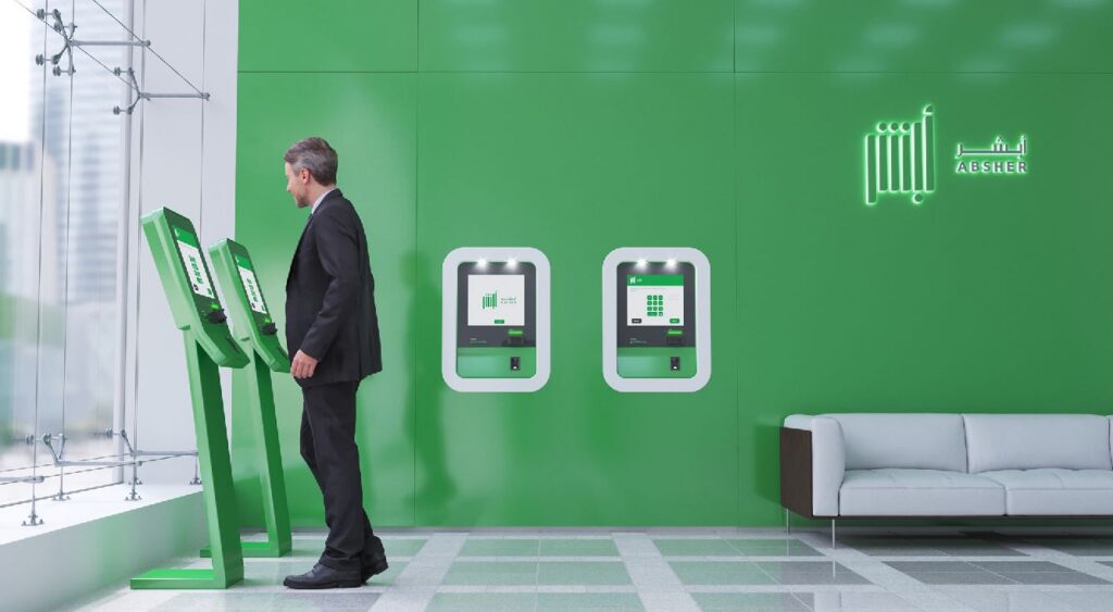 Man using a row of green self-service kiosks inside a modern, brightly lit interior with “BRASH” and Absher branding on the wall