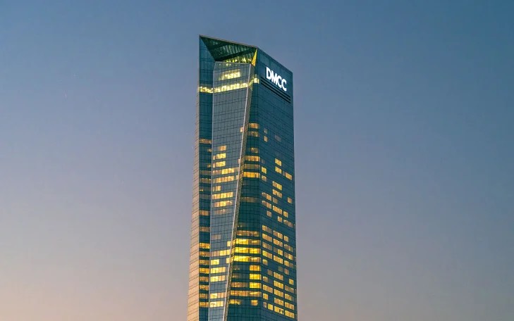Illuminated DMCC skyscraper rising into the evening sky, with office lights glowing across its glass facade.